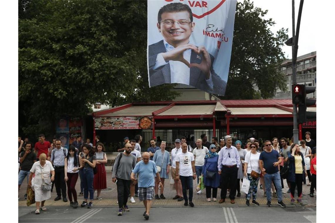 Menschen gehen unter einem Wahlplakat des Bürgermeisterkandidaten Imamoglu der Mitte-Links-Partei CHP entlang. Imamoglu hatte die Bürgermeisterwahl in Istanbul am 31. März 2019 knapp vor seinem Herausforderer Yildirim gewonnen. Allerdings annullierte die Hohe Wahlkommission die Abstimmung und ordnete eine Wiederholung am 23. Juni 2019 an. Foto: Lefteris Pitarakis/AP