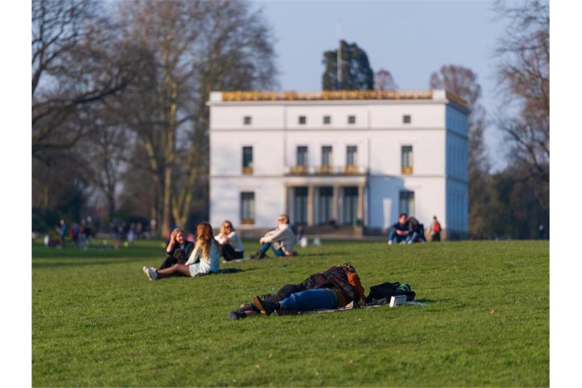 Menschen genießen das sonnige Wetter auf einer Wiese vor dem Jenisch-Haus in Hamburg. Foto: Jonas Walzberg/dpa