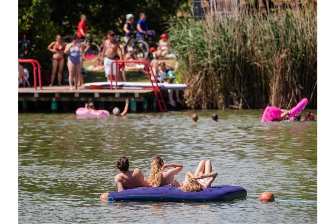 Menschen genießen den sonnigen Tag am Badesee. Foto: Christoph Schmidt/dpa/symbol