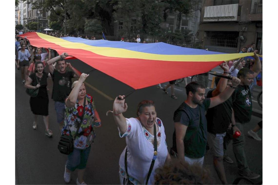Menschen halten eine rumänische Flagge während einer Demonstration zum Gedenken an ein getötetes 15-jähriges Mädchen in Bukarest. Foto: Vadim Ghirda/AP