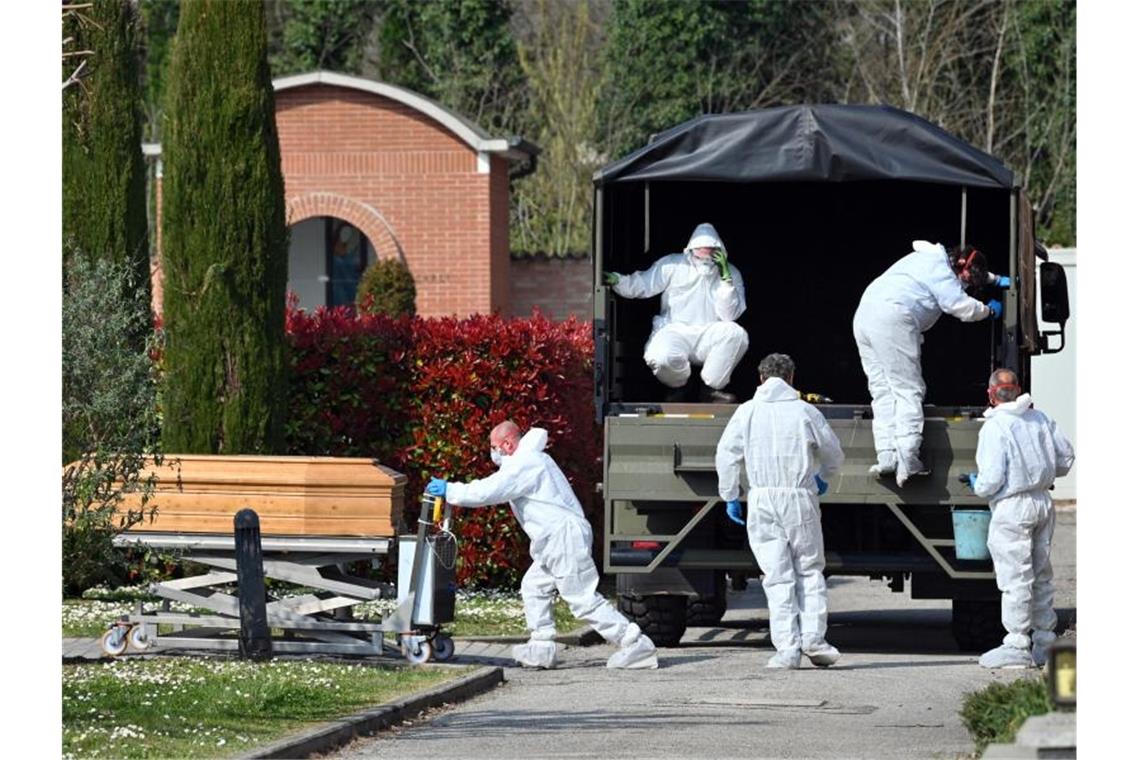 Menschen in Schutzanzügen transportieren einen Sarg auf dem Friedhof von Ferrara. Foto: Massimo Paolone/LaPresse via ZUMA Press/dpa