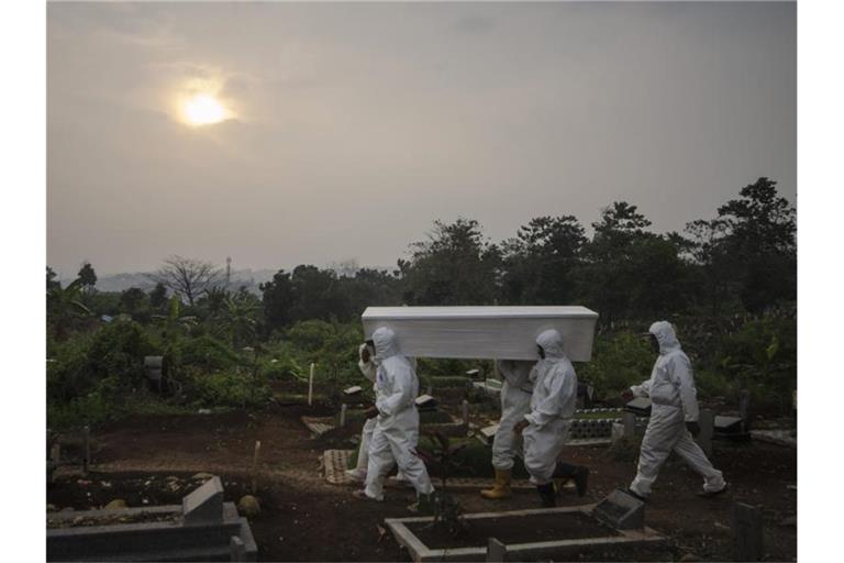 Menschen in Schutzkleidung tragen einen Sarg auf einem indonesischen Friedhof. Foto: Septianjar/XinHua/dpa