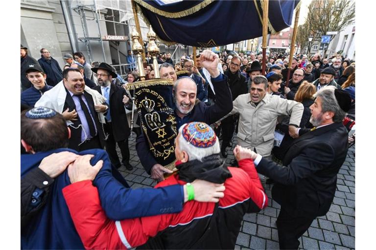 Menschen jüdischen Glaubens laufen und tanzen mit Torarollen von der alten zur neuen Synagoge. Foto: Felix Kästle/dpa