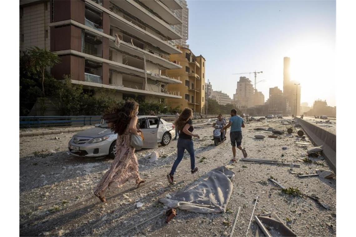 Menschen laufen nach der Explosion über eine von Trümmern übersäte Straße. Foto: Hassan Ammar/AP/dpa