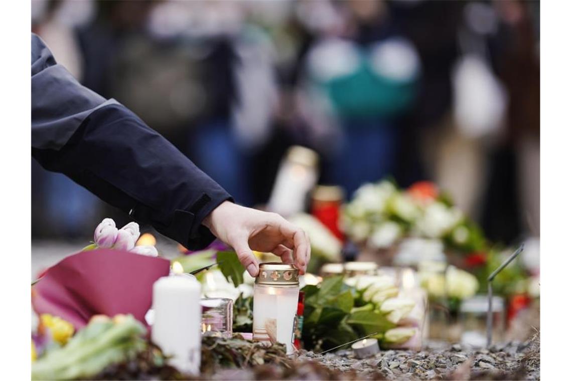 Menschen legen vor einem Gebäude der Universität Blumen und Kerzen an den Wegesrand. Foto: Uwe Anspach/dpa