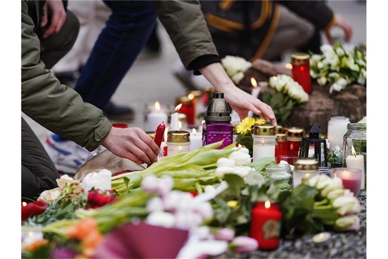 Menschen legen vor einem Gebäude der Universität Blumen und Kerzen an den Wegesrand. Foto: Uwe Anspach/dpa