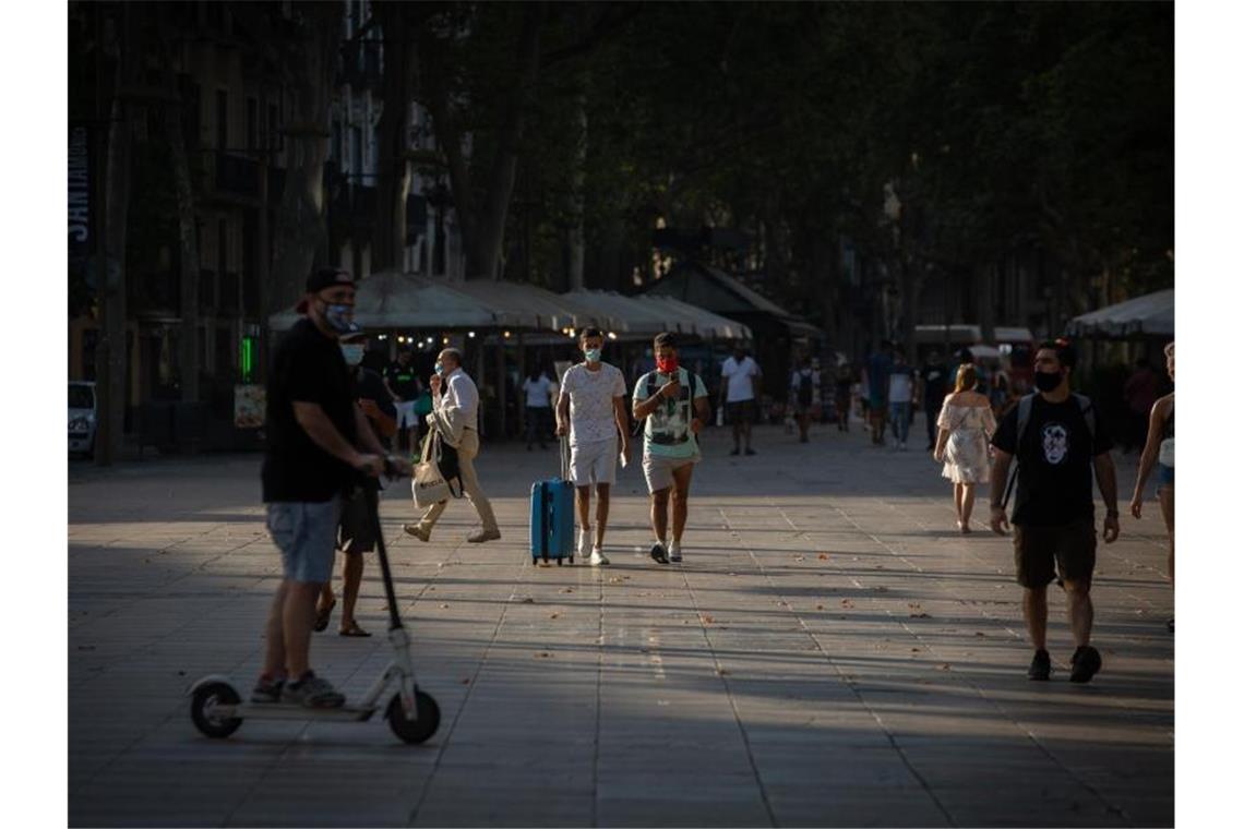 Menschen, manche von ihnen mit Mundschutz, gehen auf der langen Promenade La Rambla in Barcelona entlang. Foto: Europa Press/dpa