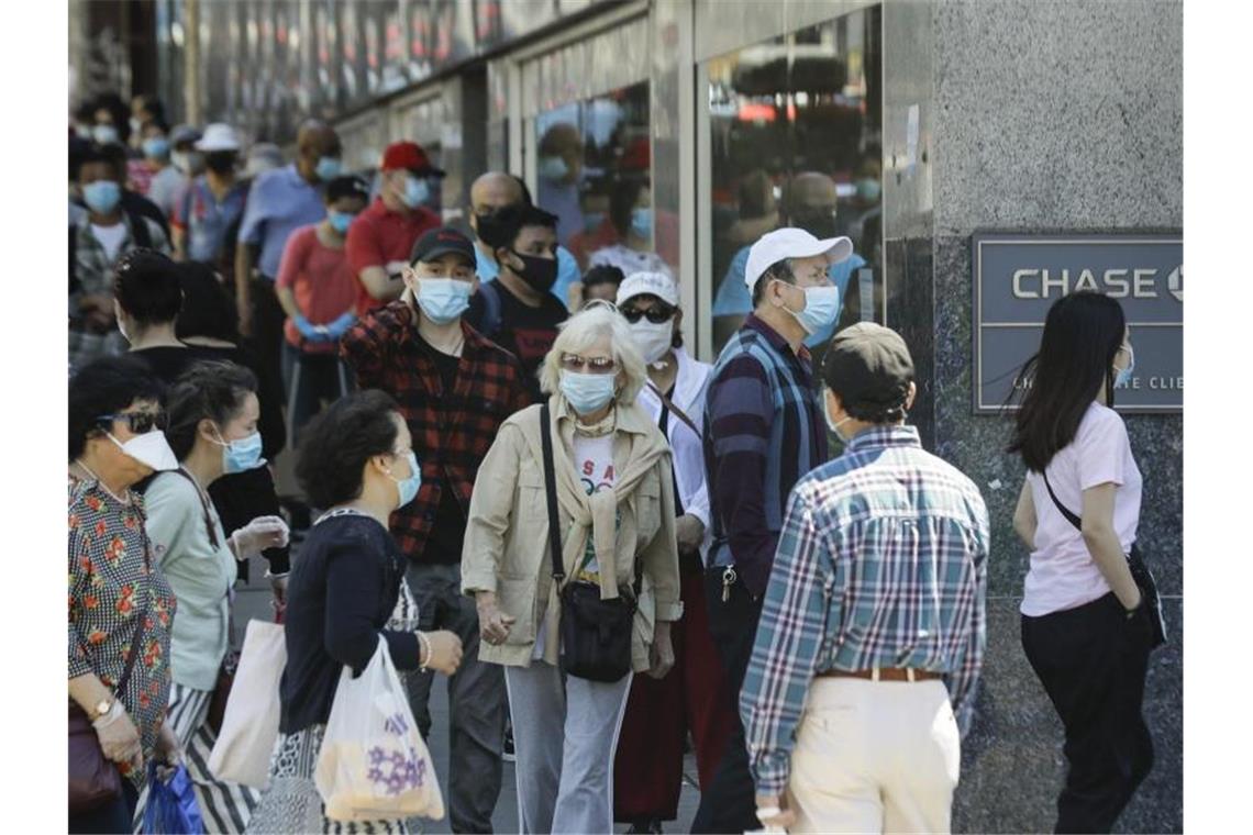 Menschen mit Masken warten im New Yorker Stadtbezirk Queens vor dem Eingang einer Bank. Foto: Frank Franklin Ii/AP/dpa