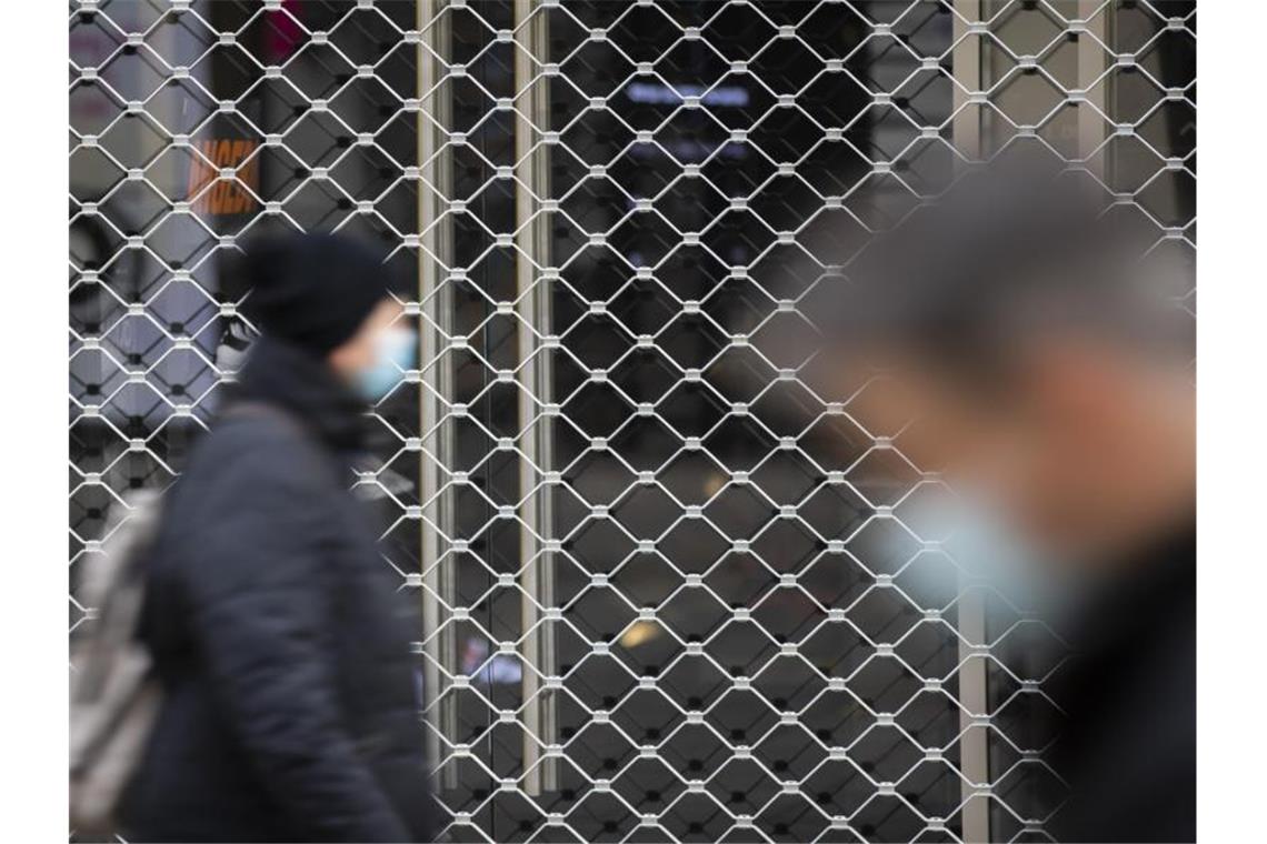 Menschen mit Mundschutz gehen an einem geschlossenen Geschäft in der Königsstraße in Stuttgart vorbei. Foto: Tom Weller/dpa