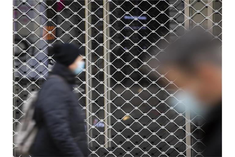 Menschen mit Mundschutz gehen an einem geschlossenen Geschäft in der Stuttgarter Innenstadt vorbei. Foto: Tom Weller/dpa