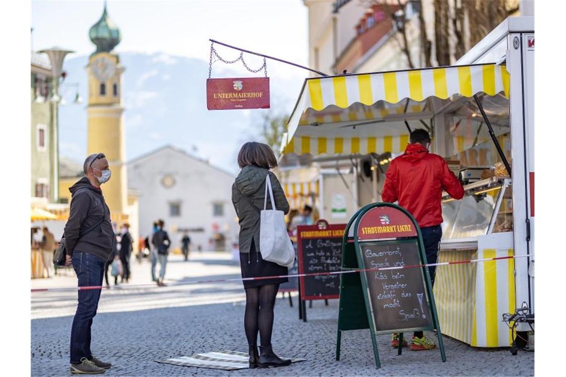 Menschen mit Mundschutz stehen an einem Marktstand in Lienz im Tirol an. Foto: Expa/ Johann Groder/APA/dpa