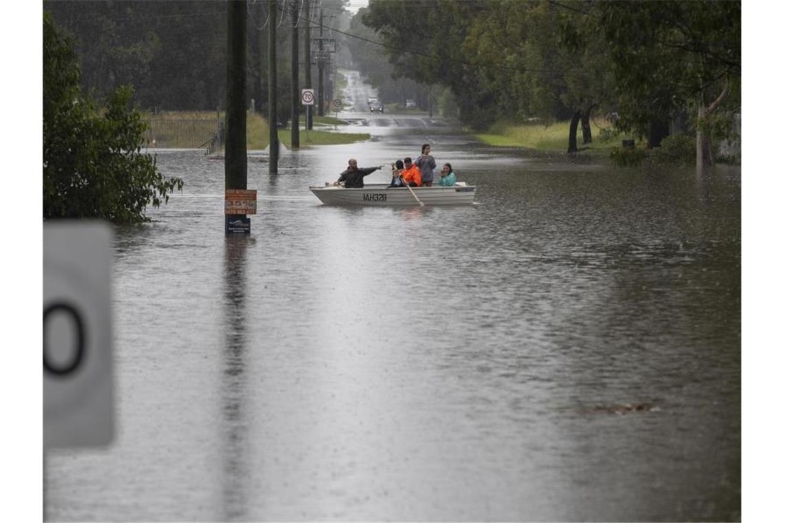 Menschen paddeln mit ihrem Boot durch das Wasser in einem Vorort von Sydney. Foto: Mark Baker/AP/dpa