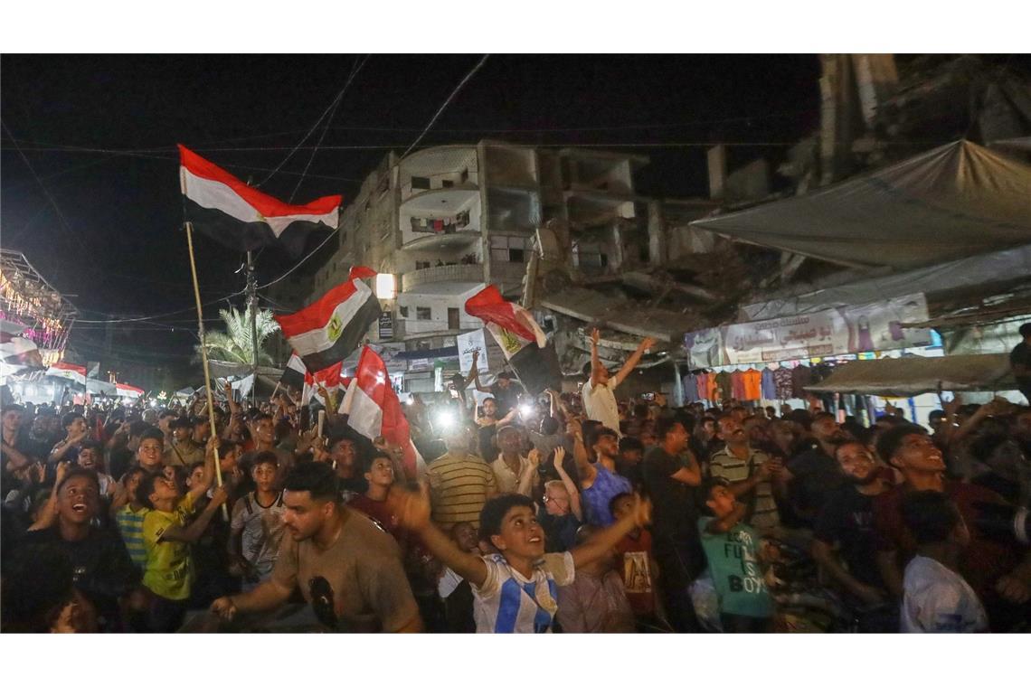 Menschen schwenke agyptische Flaggen und verfolgen im zentralen Gazastreifen das WM-Spiel Ägypten gegen Belgien auf einer Großbildleinwand.