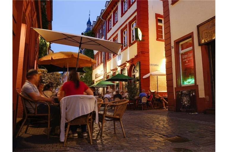 Menschen sitzen am Abend in der Heidelberger Innenstadt vor Kneipen in der Unteren Straße. Foto: Uwe Anspach/dpa/Archivbild