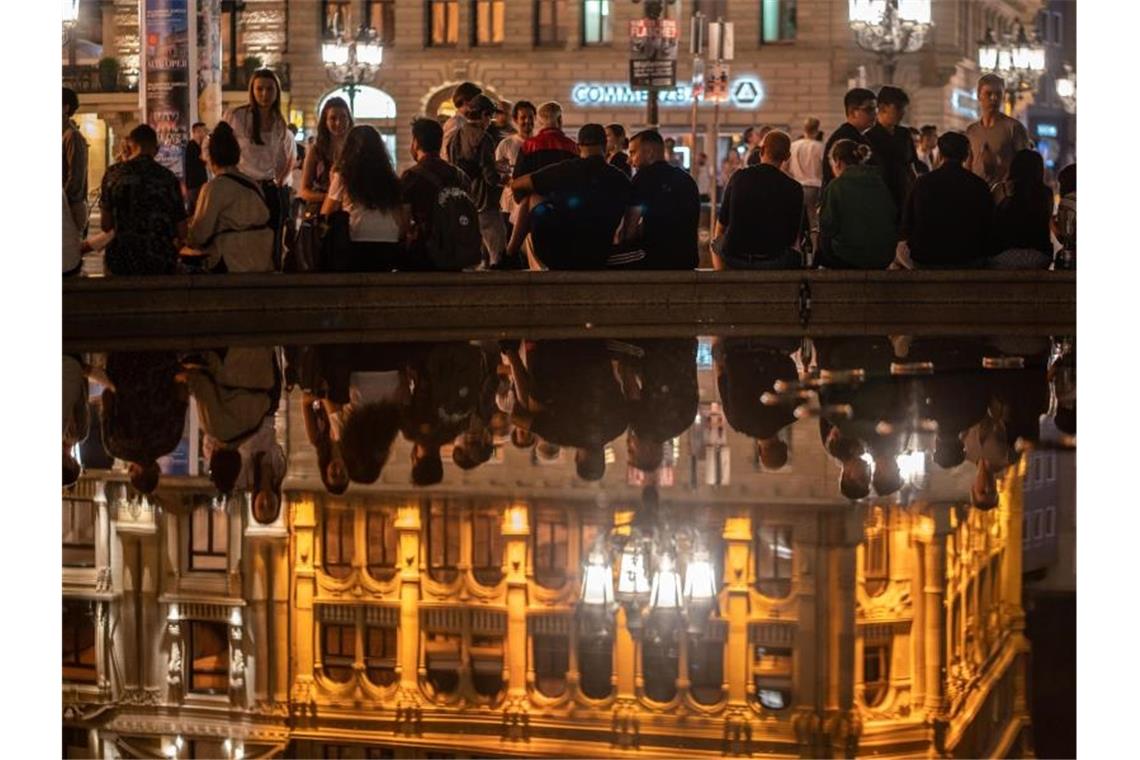 Menschen sitzen am Brunnen vor der Alten Oper in Frankfurt. Dort wurde in der Nacht nur friedlich gefeiert. Foto: Frank Rumpenhorst/dpa