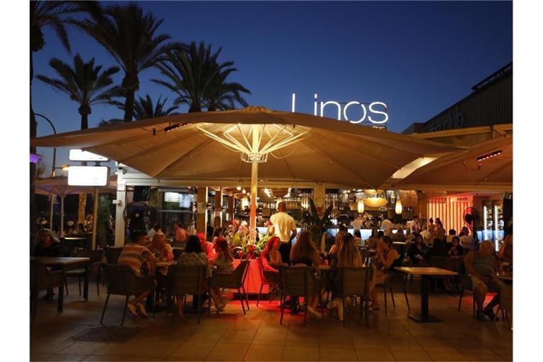 Menschen sitzen in einer Bar an der Strandpromenade von Palma. Foto: Clara Margais/dpa