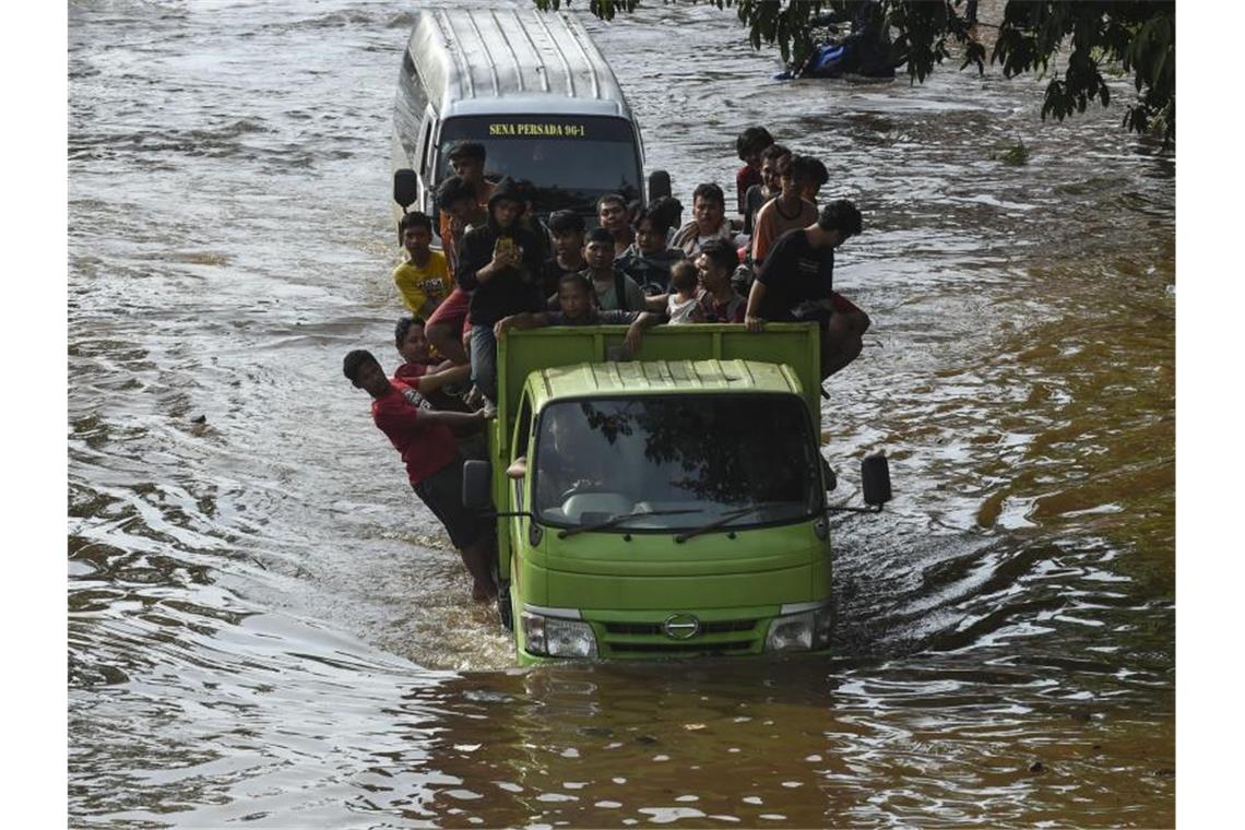 Menschen stehen auf der Ladefläche eines Transporters, um eine überflutete Straße in Jakarta zu passieren. Foto: Agung Kuncahya B./XinHua/dpa