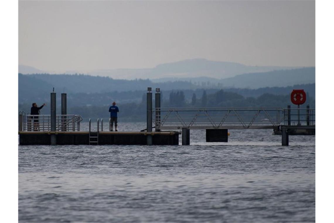 Menschen stehen auf einem Steg am Ufer des Bodensees in Sipplingen. Foto: Marijan Murat/Archivbild