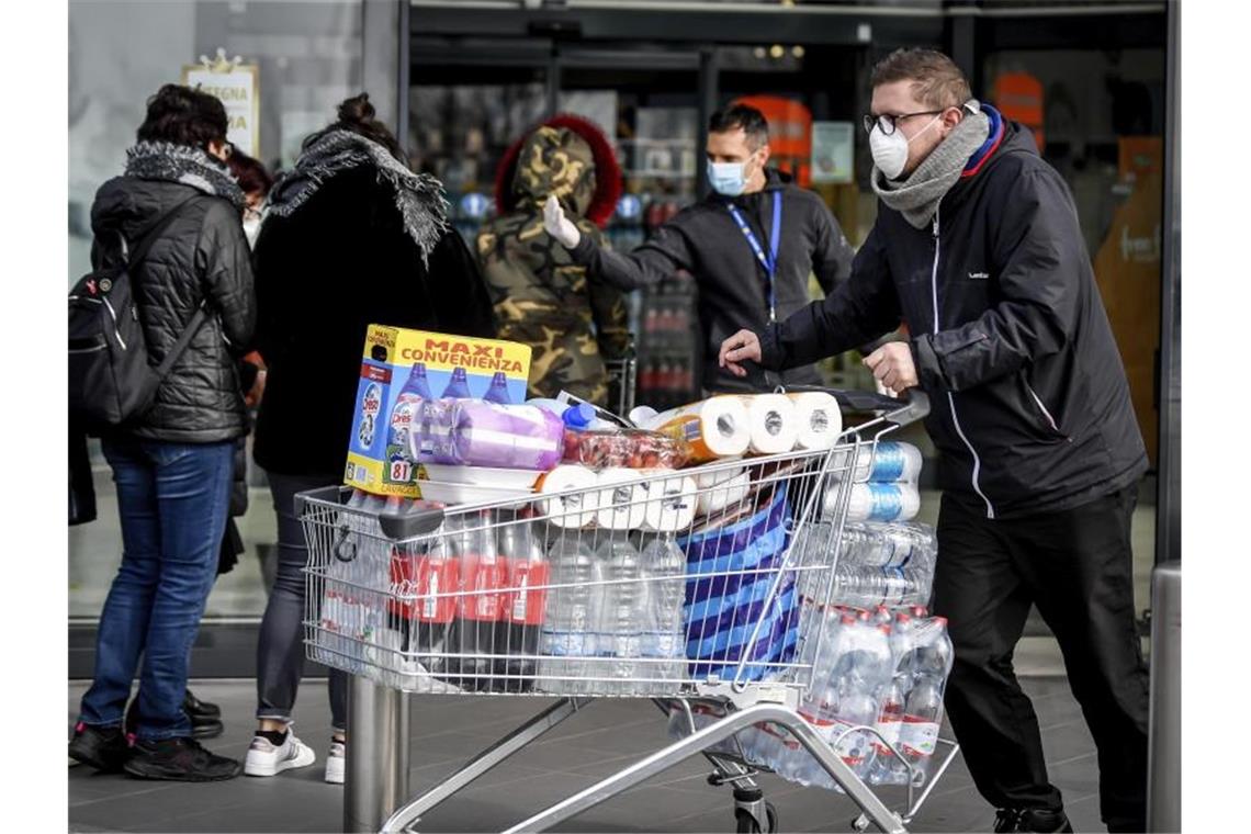 Menschen stehen mit Atemschutzmasken vor einem Supermarkt in der Lombardei. In einzelnen Gebieten Norditaliens ist das öffentliche Leben teilweise zum Erliegen gekommen. Foto: Claudio Furlan/LaPresse/AP/dpa