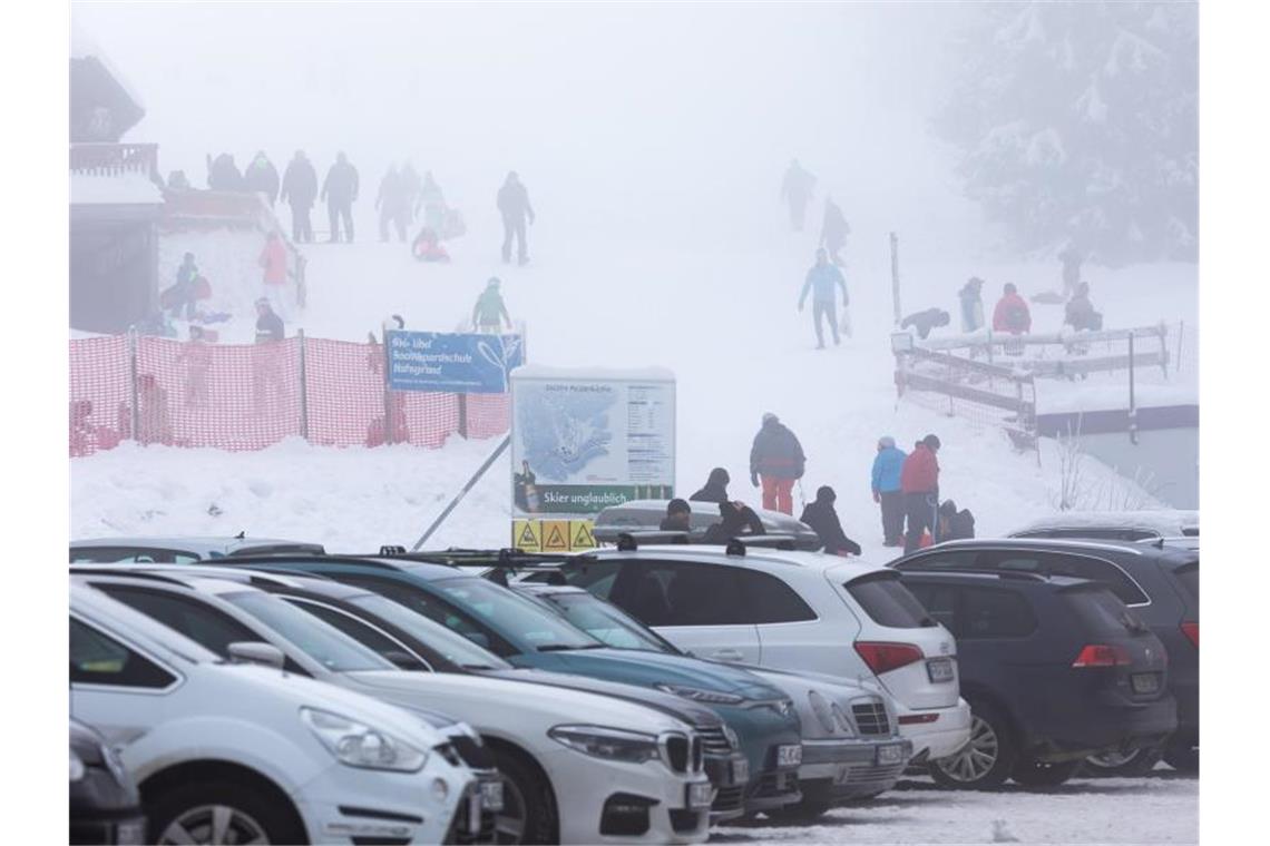 Bergwacht appelliert: Zufahrten und Rettungswege frei halten Menschen stehen neben einem Skilift am Haldenköpfle und vollen Parkplätzen. Foto: Philipp von Ditfurth/dpa/Archivbild