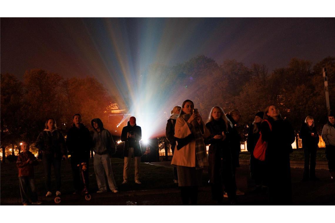 Menschen stehen vor einem Beamer, während der Berliner Dom bei der Generalprobe für das 21. Festival of Lights Berlin unter dem Motto „Let’s Shine Together“ angestrahlt wird.