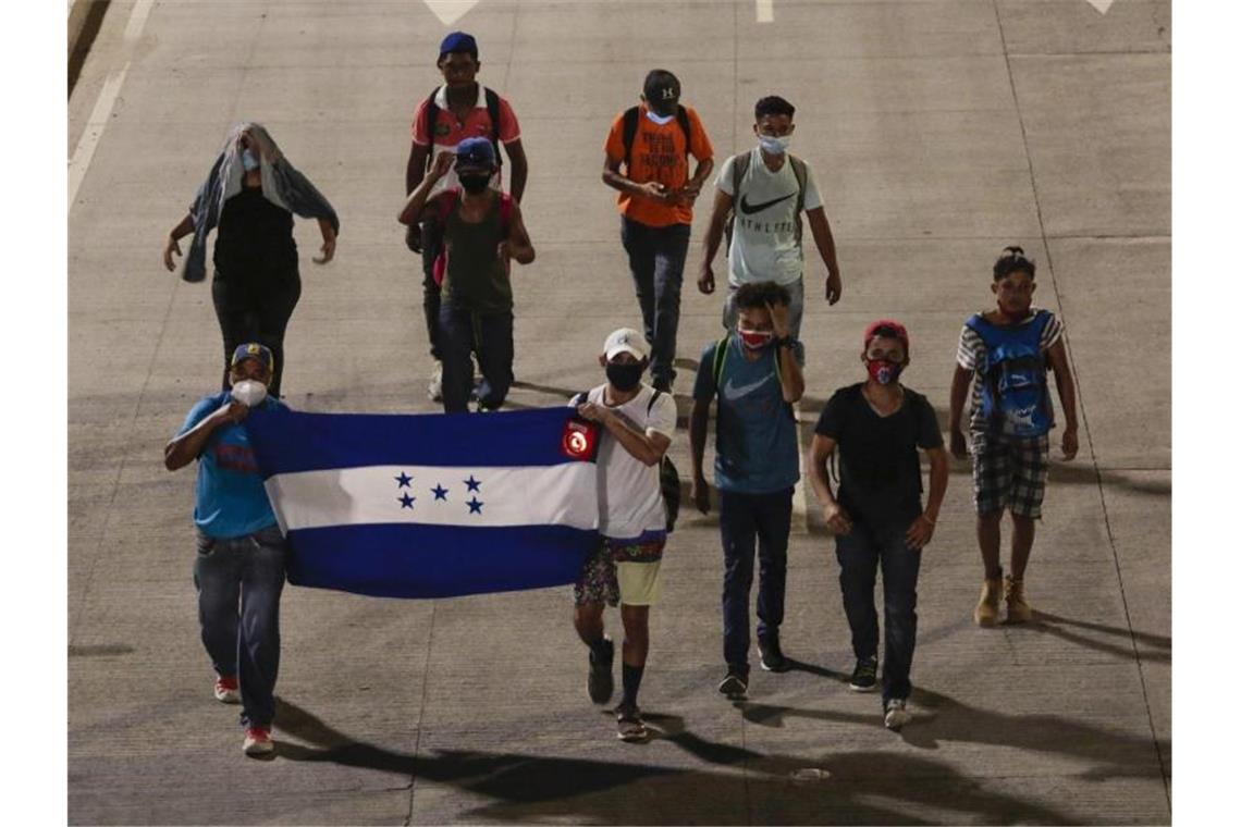 Menschen tragen eine Fahne von Honduras und gehen in der Hoffnung, zukünftig die USA zu erreichen, einen Highway entlang. Foto: Uncredited/AP/dpa