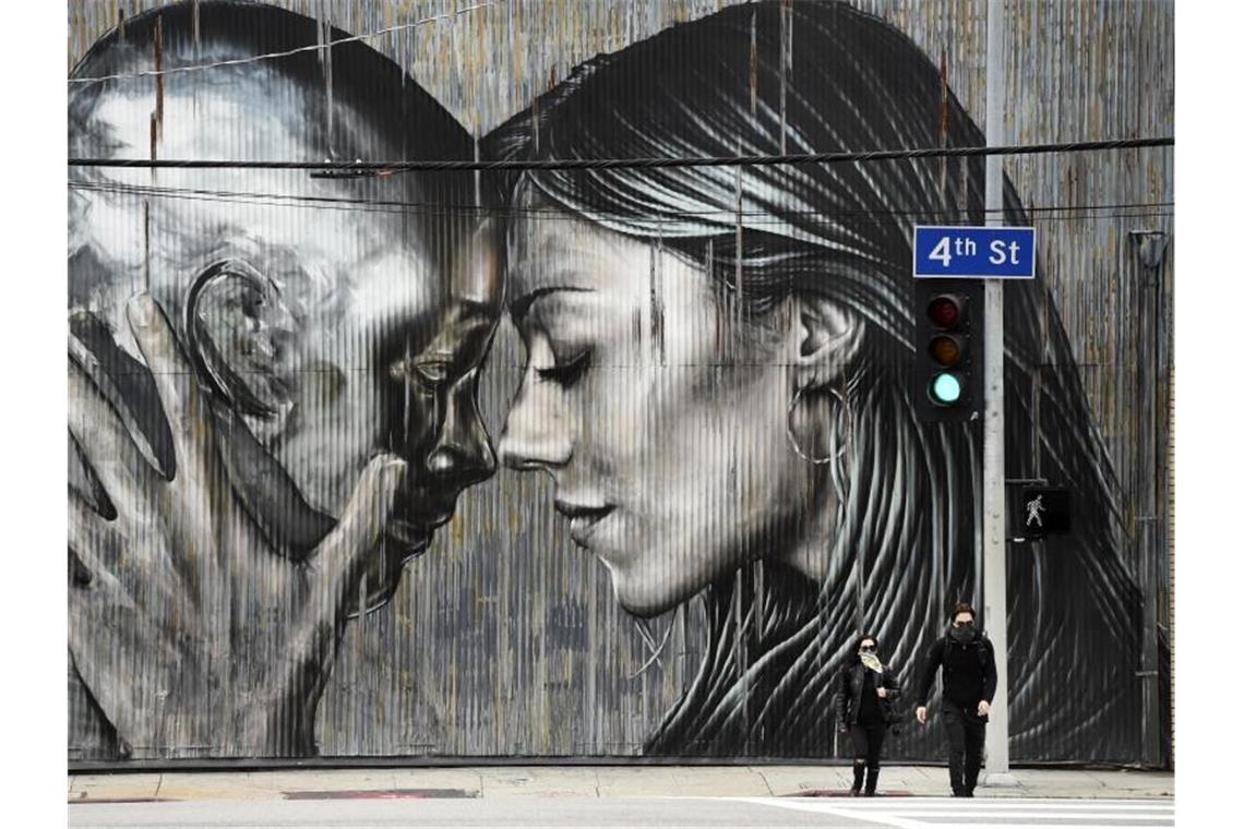 Menschen tragen einen Mundschutz, während sie eine Straße vor einem Wandbild in Los Angeles überqueren. Foto: Chris Pizzello/AP/dpa