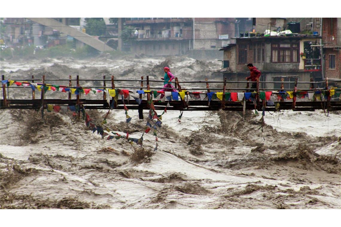 Menschen wagen im nordindischen Bundesstaat Himachal Pradesh trotz schwerer Überschwemmungen den Weg über eine Brücke, um den Fluss Beas zu überqueren.