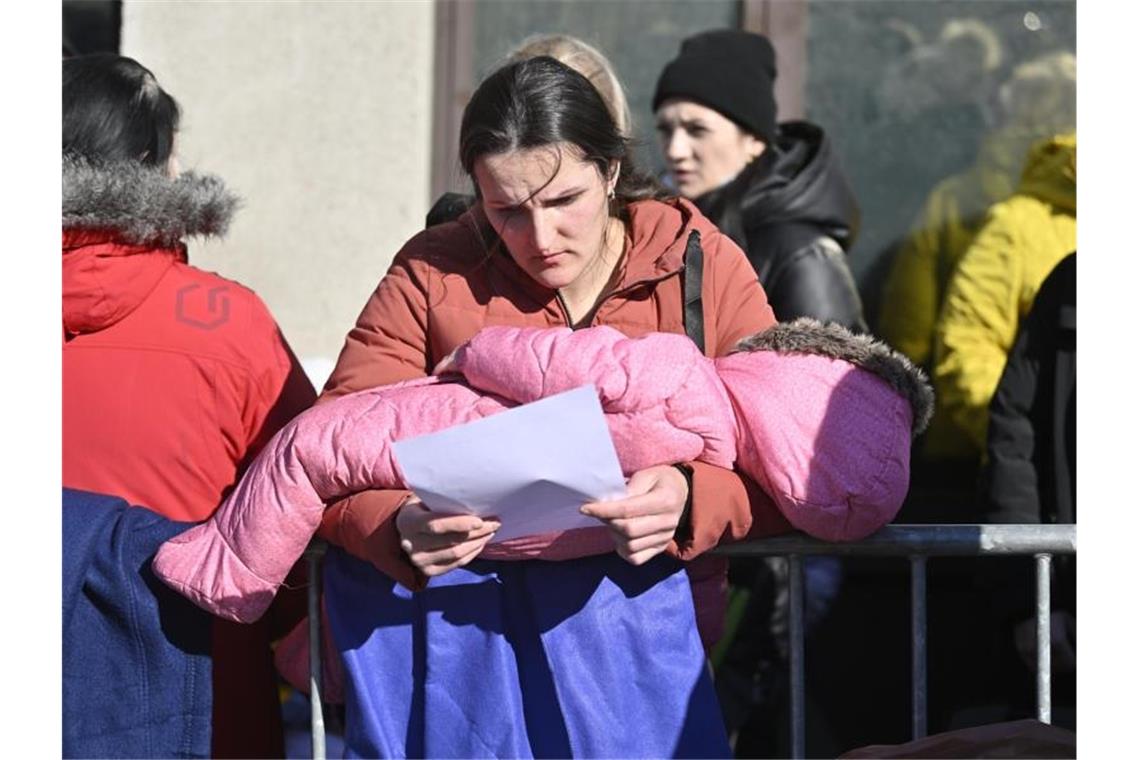 Menschen wartet mit einem Kind im Arm vor einem Zentrum zur Registrierung und Unterbringung von Geflüchteten in Brüssel. Foto: Eric Lalmand/BELGA/dpa