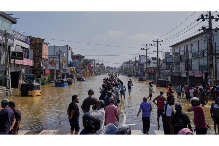 Menschen waten durch ein überschwemmtes Gebiet in Sri Lanka.