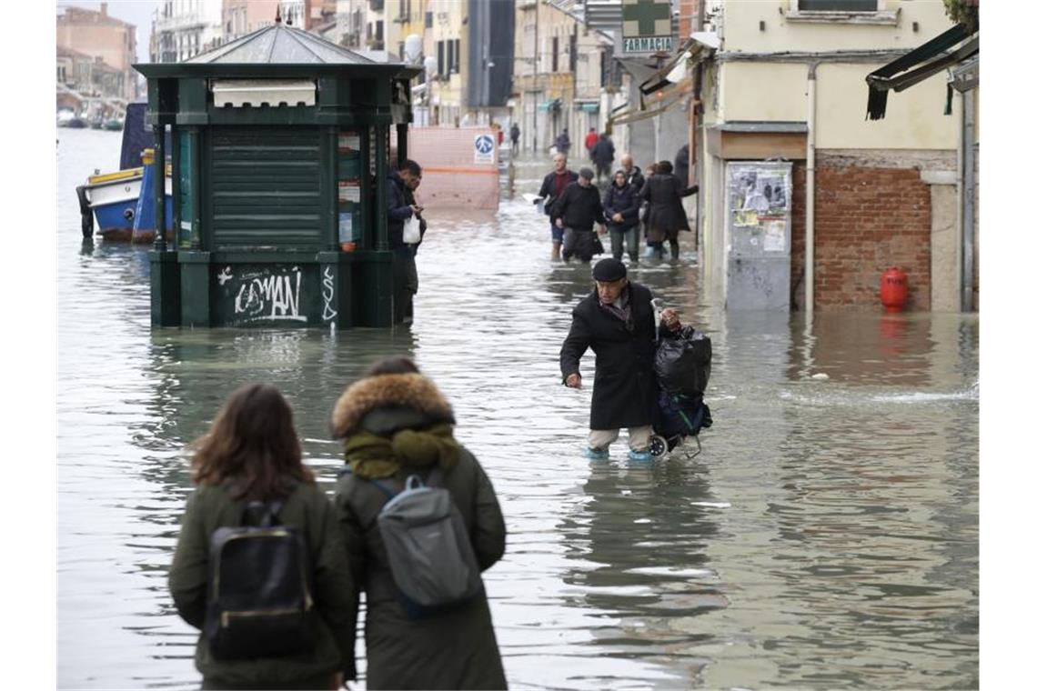 Menschen waten durch eine überflutete Straße. Bürgermeister Luigi Brugnaro spricht von einer „Katastrophe“ und macht den Klimawandel für das Hochwassser verantwortlich. Foto: Luca Bruno/AP/dpa