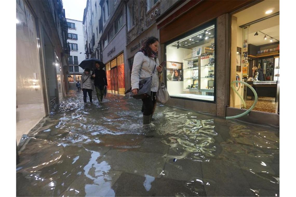 Menschen waten in Gummistiefeln durch Hochwasser in einer Gasse in Venedig. Foto: Andrea Merola/ANSA/AP/dpa
