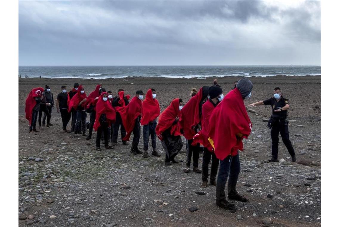 Migranten aus Marokko stehen an einem Strand auf Gran Canaria, nachdem sie den Atlantik mit einem Holzboot überquert haben. Foto: Javier Bauluz/AP/dpa