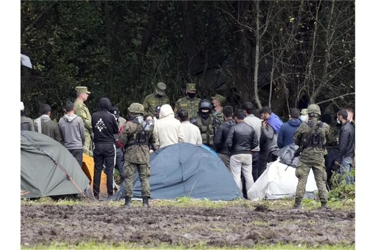 Migranten, die an der Grenze zu Belarus festsitzen, werden von polnischen Beamten umstellt. Foto: Czarek Sokolowski/AP/dpa