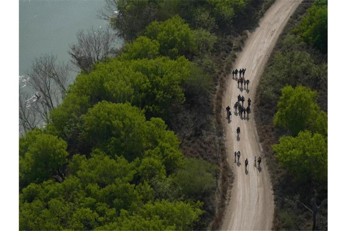 Migranten gehen einen Feldweg in Mission (Texas) entlang, nachdem sie die Grenze zwischen Mexiko und den USA überquert haben. Foto: Julio Cortez/AP/dpa