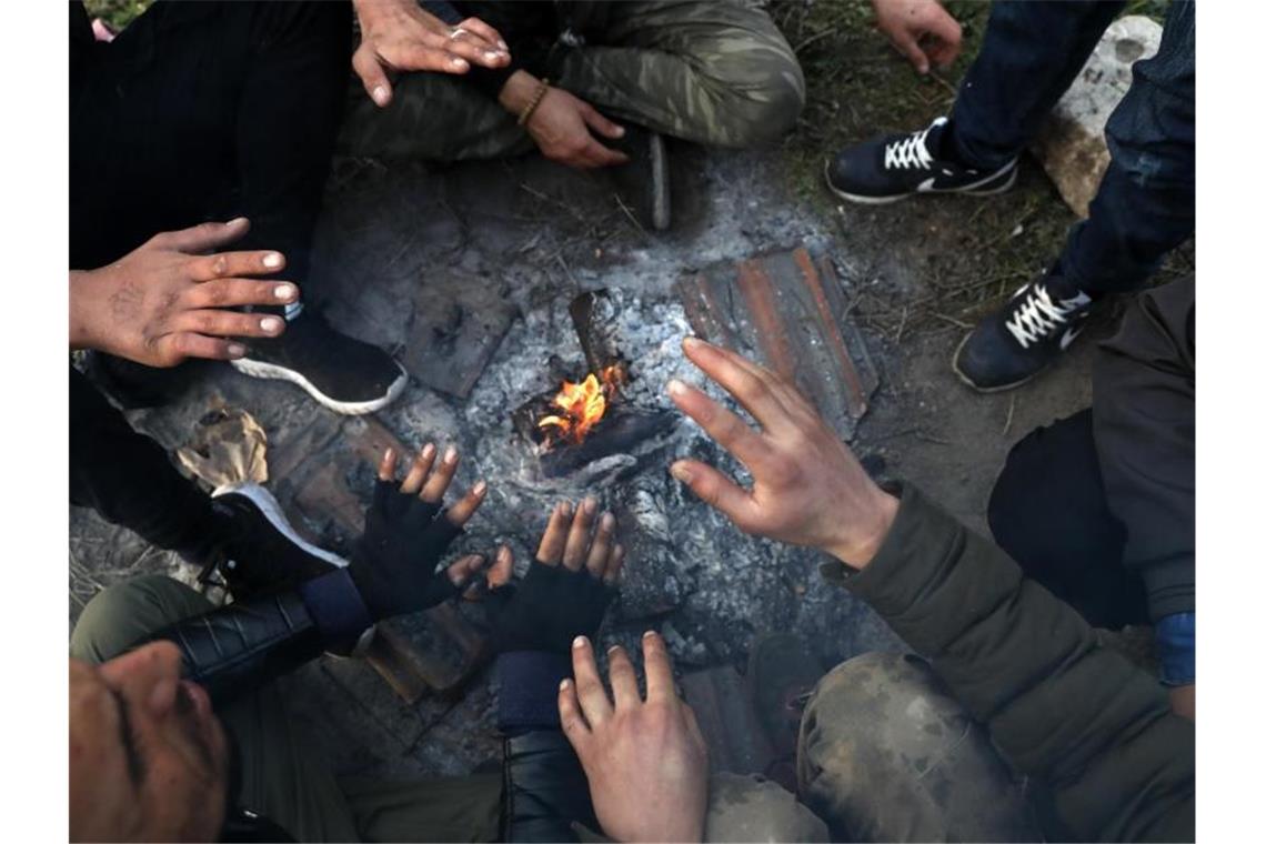 Migranten sitzen nahe der türkisch-griechischen Grenze um ein Lagerfeuer herum und versuchen, sich zu wärmen. Foto: Darko Bandic/AP/dpa