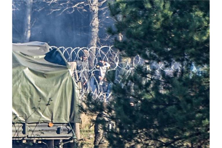 Migranten stehen an der Grenze zwischen Polen und Belarus nahe des Grenzübergangs Kusnica hinter Stacheldrahtrollen. Foto: Michael Kappeler/dpa