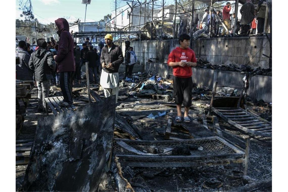 Migranten stehen auf den abgebrannten Überresten des Gemeinschaftszentrums. Foto: Panagiotis Balaskas/AP/dpa