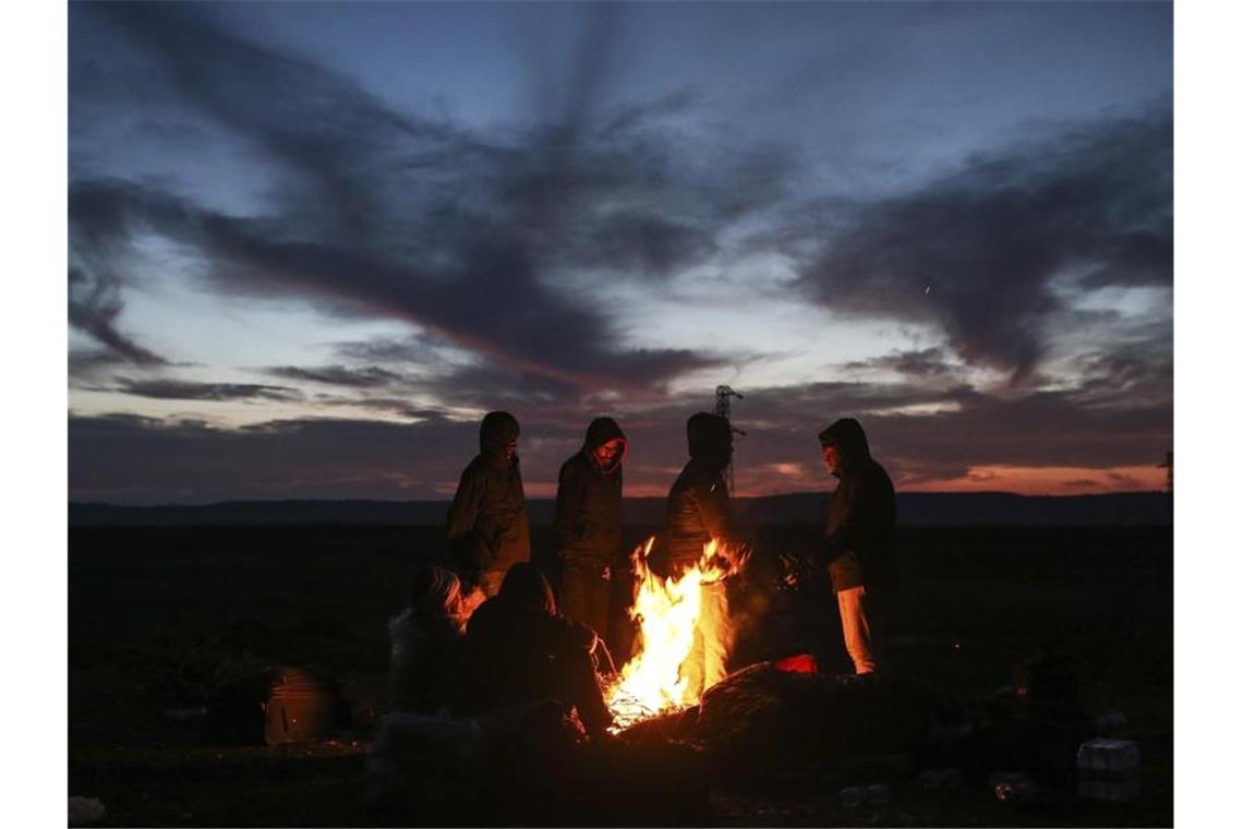 Migranten wärmen sich in der Nähe eines Grenzübergangs an einem Lagerfeuer. Foto: Emrah Gurel/AP/dpa