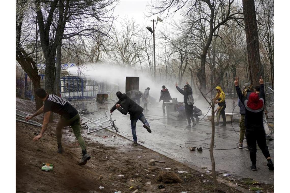 Migranten werfen Steine, die griechische Polizei setzt einen Wasserwerfer ein. Foto: Ismail Coskun/IHA/dpa