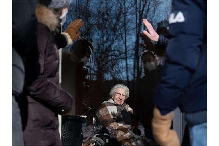 Mina Hehn sitzt an ihrem 108. Geburtstag hinter einer Terassentür, während Angehörige ihr winken. Foto: Marijan Murat/dpa