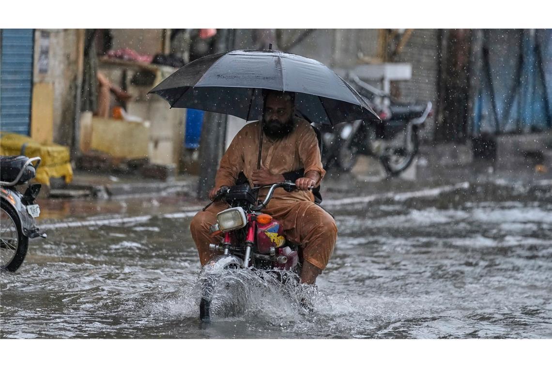 Bilder des Tages Mit aufgespanntem Regenschirm fährt ein Motorradfahrer waghalsig durch die Monsunfluten.