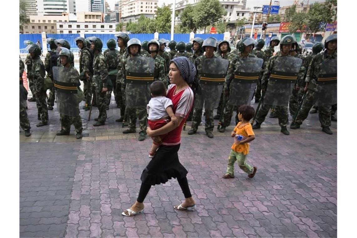 Geheimdokumente enthüllen Verfolgung von Uiguren in China Mit einem Baby auf dem Arm passiert eine Frau der uigurischen Minderheit eine Reihe von Soldaten. Foto: Azubel/epa/dpa/Archiv