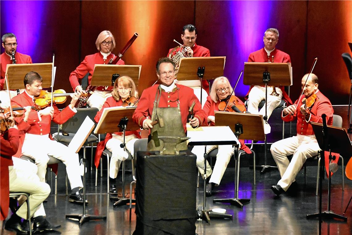 Mit zwei Hämmern bearbeitet Dirigent Rainer Roos bei der Polka „Feuerfest!“ einen Amboss.