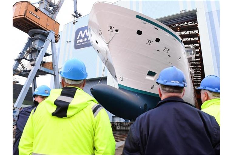 Mitarbeiter beobachten, wie ein Neubau auf der Stralsunder MV Werft eine Schiffbauhalle verlässt. Foto: Stefan Sauer/dpa-Zentralbild/dpa