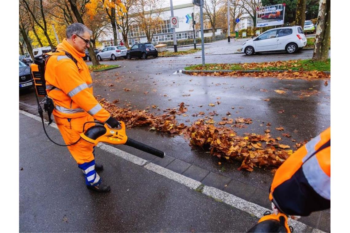 Mitarbeiter der Straßenreinigung blasen mit Laubbläsern nasses Laub auf die Straße. Foto: Philipp von Ditfurth/dpa