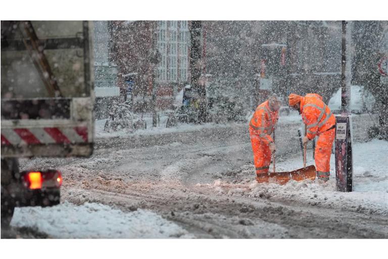 Mitarbeiter des Winterdienstes räumen in Hamburg den Schnee von einem schneebedeckten Zebrastreifen und Fußgängerübergang.