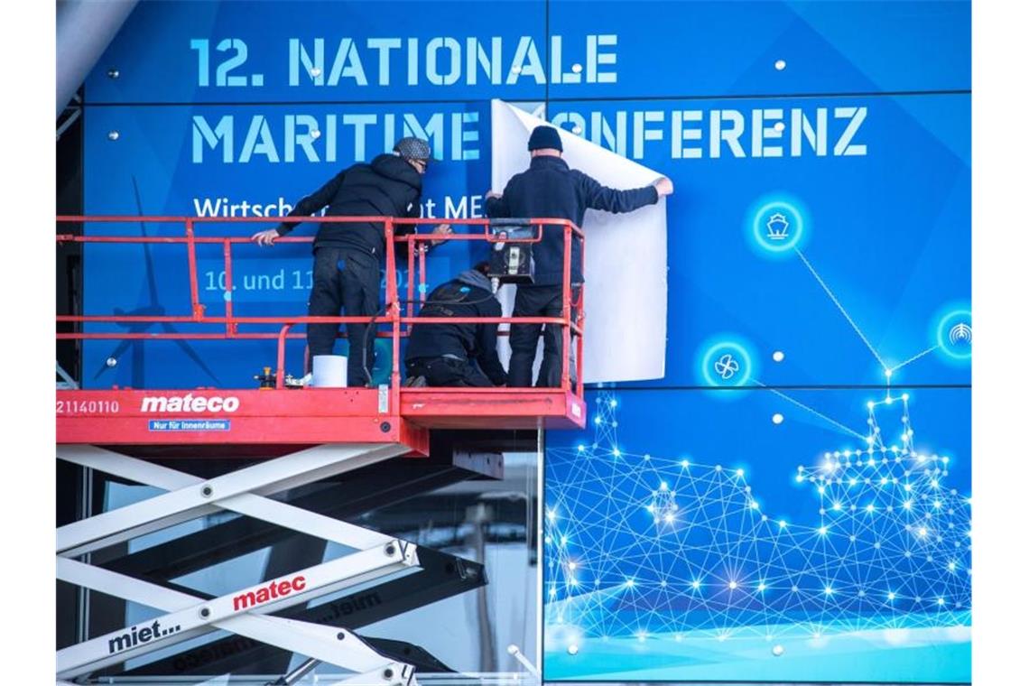 Mitarbeiter einer Werbefirma kleben am Cruise Center in Warnemünde ein Plakat für die 12. Nationale Maritime Konferenz. Foto: Jens Büttner/dpa-Zentralbild/dpa