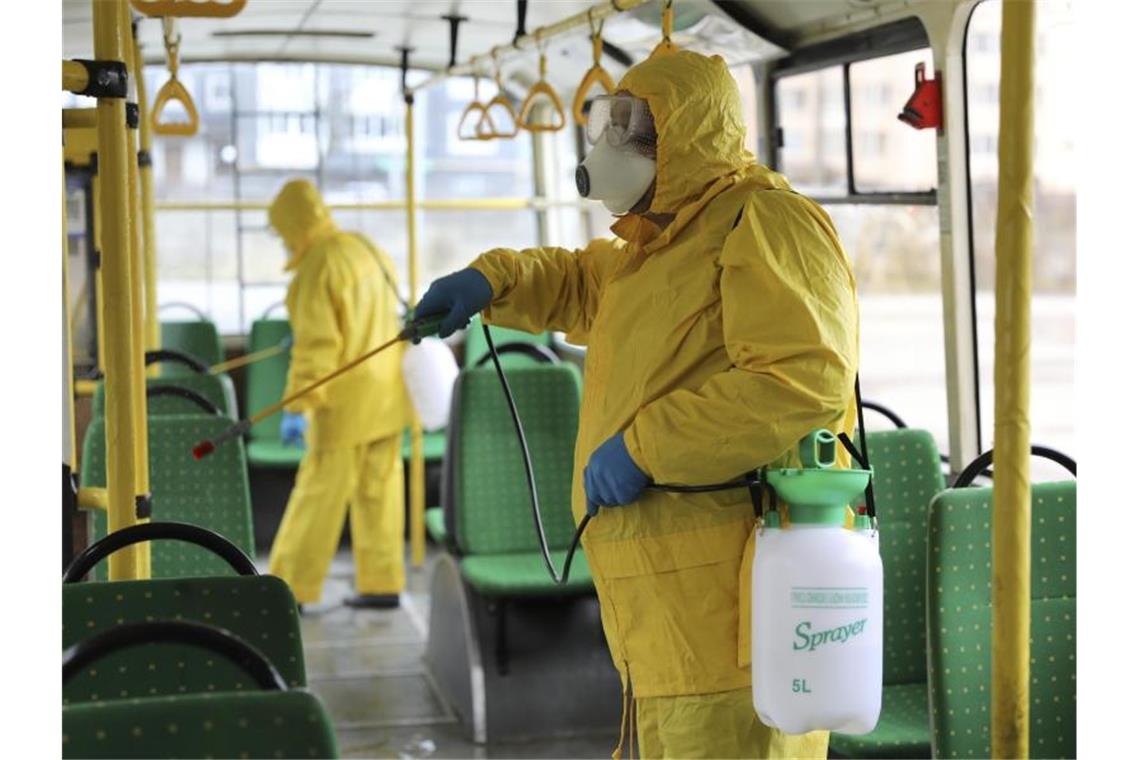 Mitarbeiter in Schutzausrüstung versprühen im ukrainischen Lwiw Desinfektionsmittel in einem Bus. Foto: Mykola Tys/AP/dpa