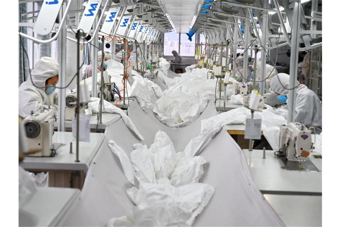 Mitarbeiter tragen Mundschutz in einer Produktionhalle eines Unternehmens zur Fertigung von Schutzanzügen. Foto: Lin Shanchuan/XinHua/dpa